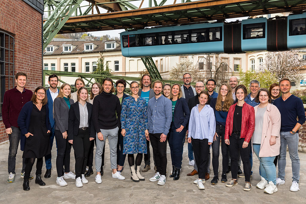 Team Gruppenfoto Firma mit Schwebebahn im Hintergrund